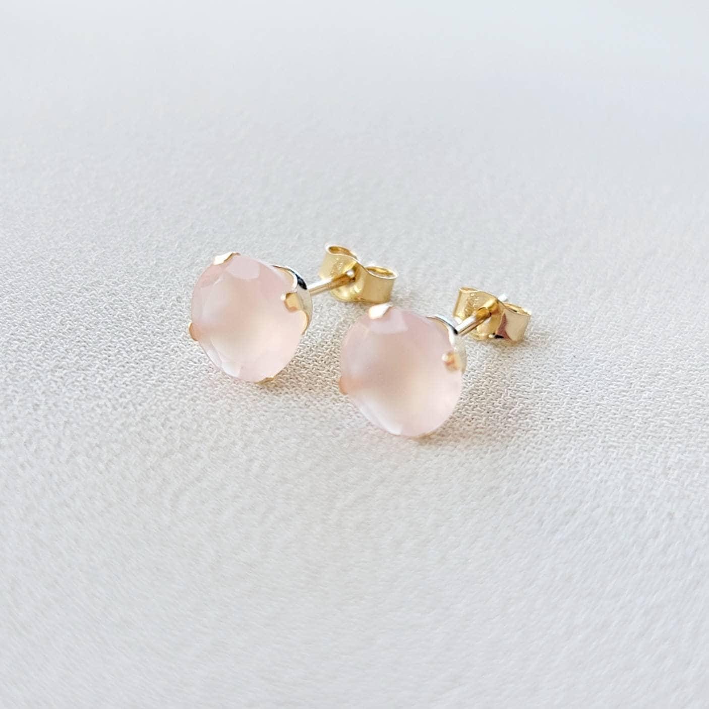 A pair of gold stud earrings with pink gemstone accents. The earrings are made of 14k gold and feature a round, faceted gemstone in a prong setting.