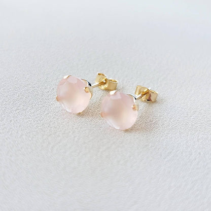 A pair of gold stud earrings with pink gemstone accents. The earrings are made of 14k gold and feature a round, faceted gemstone in a prong setting.