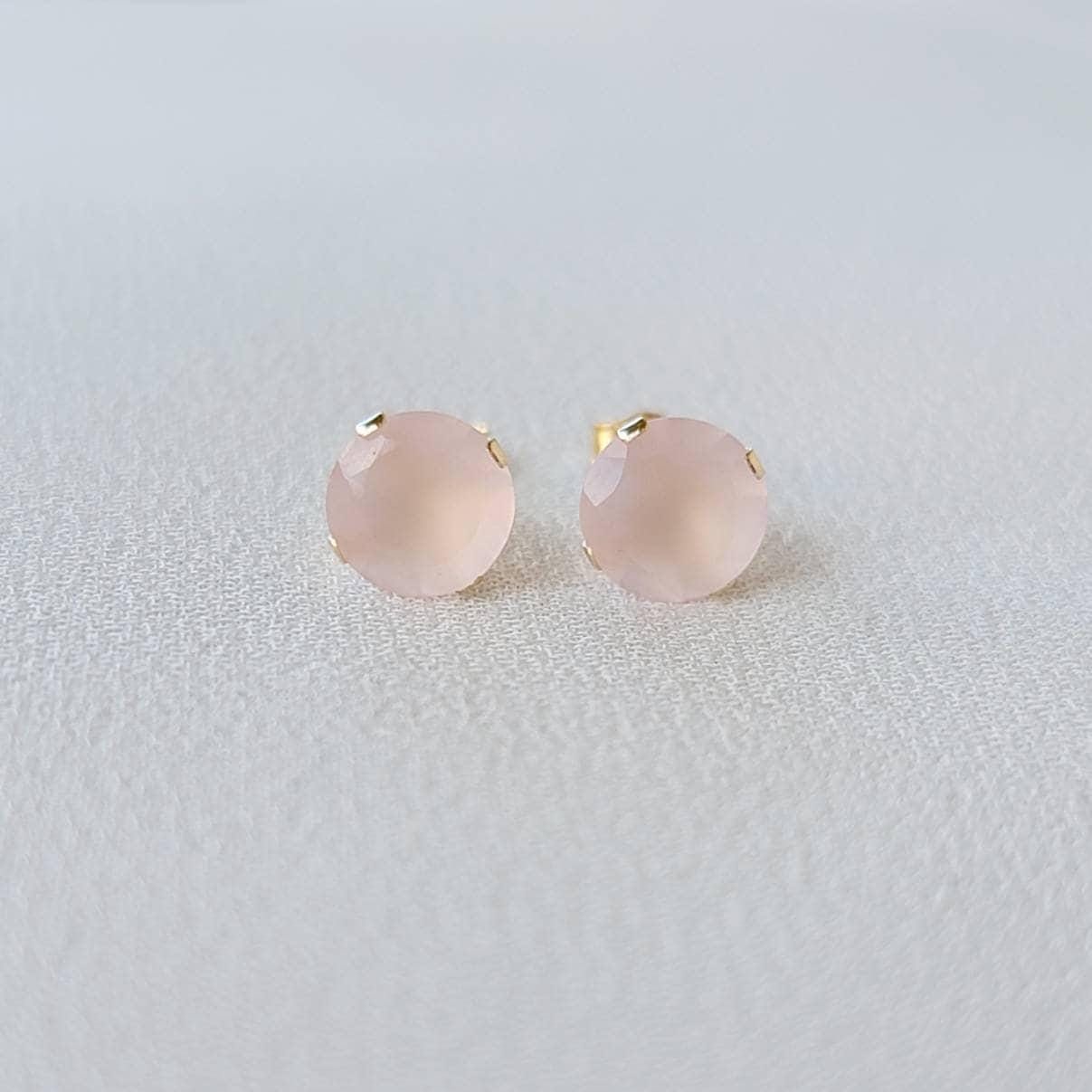A pair of gold stud earrings with pink gemstone accents. The earrings are made of 14k gold and feature a round, faceted gemstone in a prong setting.
