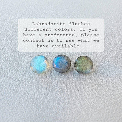 Three round labradorite gemstones, one blue, one gray, and one green, on a white textured surface. Labradorite flashes different colors. If you have a preference, please contact us to see what we have available.