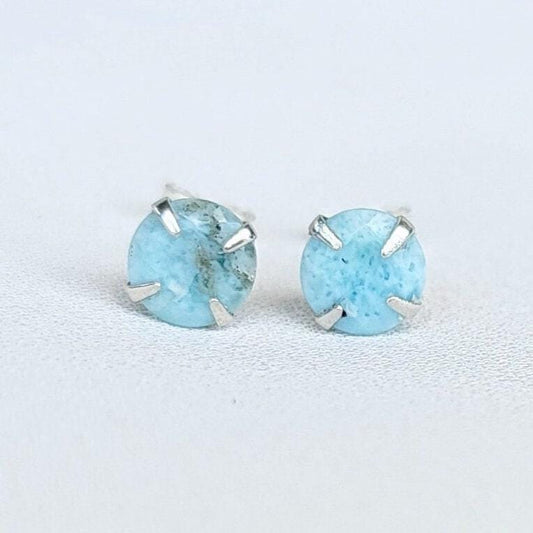 A pair of silver stud earrings with light blue Larimar round gemstones. The gemstones have a speckled pattern.
