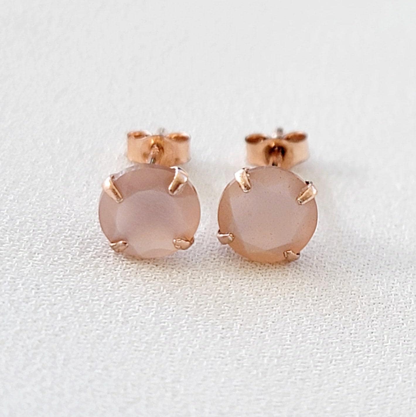 A pair of rose gold stud earrings with a light pink round shaped peach moonstone in each earring.