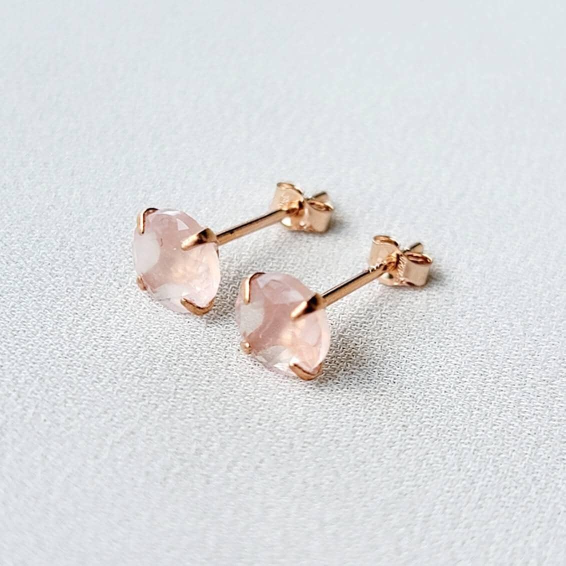Rose gold stud earrings featuring round faceted rose quartz gemstones. Each earring showcases a light pink, translucent stone securely set in a four-prong rose gold setting. The posts and butterfly backs are also crafted from rose gold, ensuring a cohesive and elegant look. These delicate earrings are perfect for adding a touch of understated glamour to any outfit.