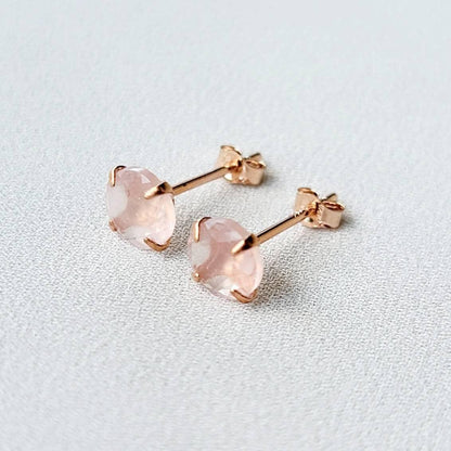 Rose gold stud earrings featuring round faceted rose quartz gemstones. Each earring showcases a light pink, translucent stone securely set in a four-prong rose gold setting. The posts and butterfly backs are also crafted from rose gold, ensuring a cohesive and elegant look. These delicate earrings are perfect for adding a touch of understated glamour to any outfit.