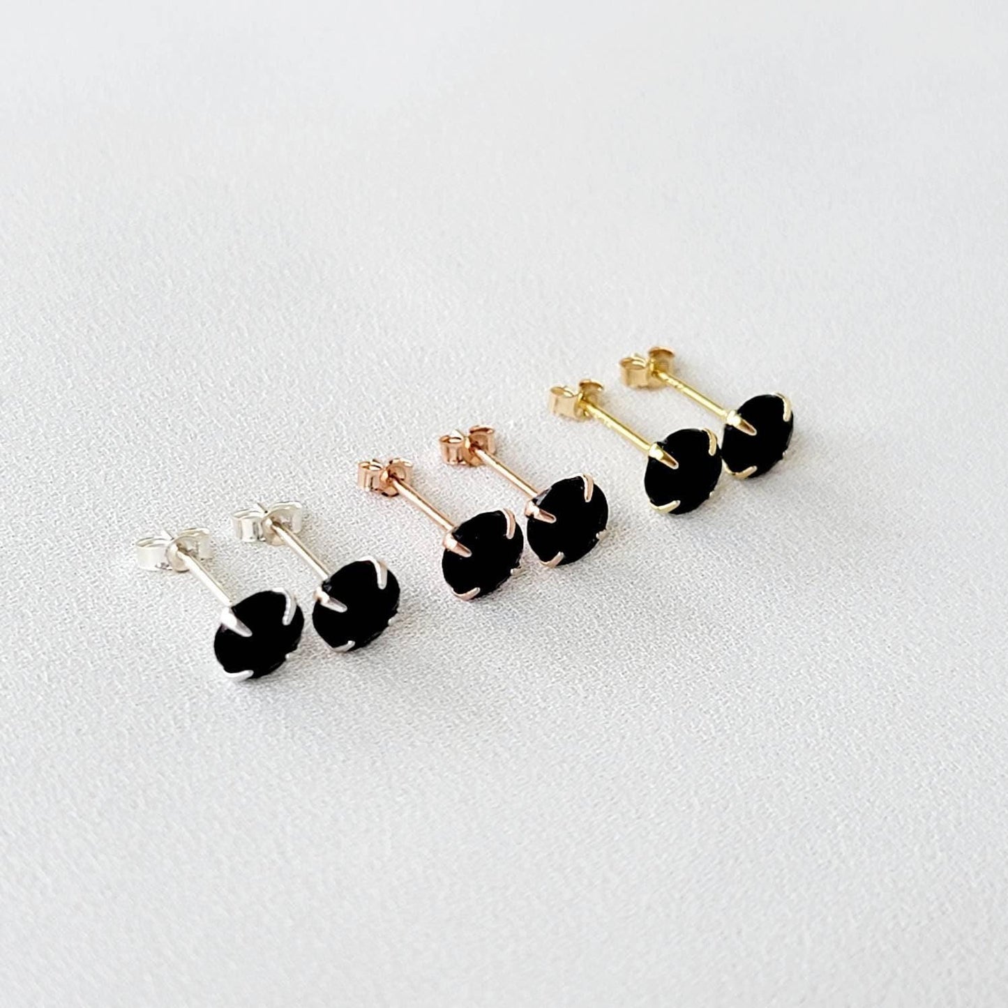 A pair of gold stud earrings with round faceted black onyx gemstones.
