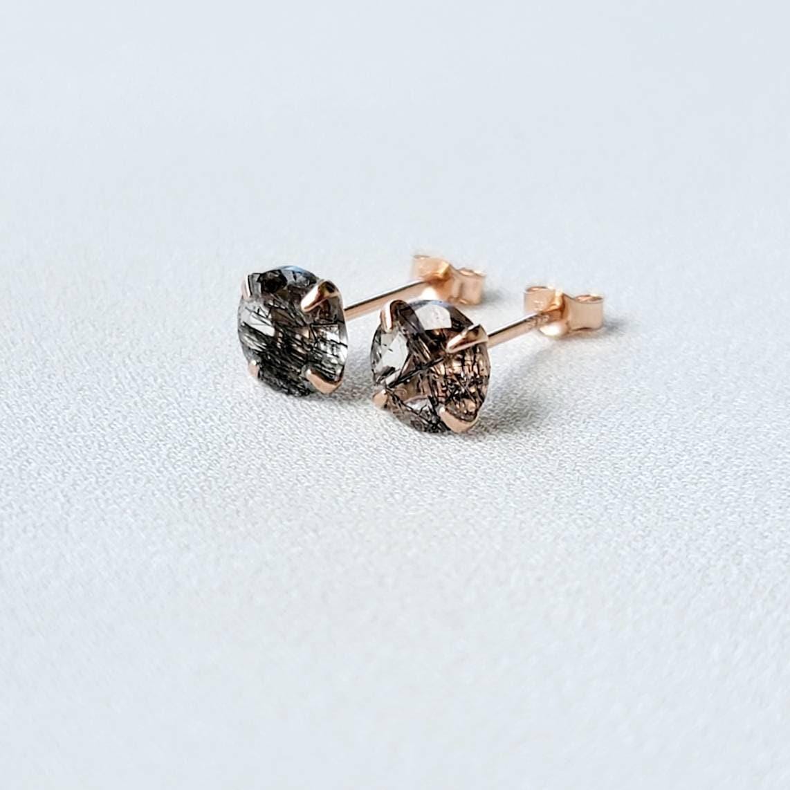 A pair of rose gold stud earrings with black spikes going through clear quartz. The earrings are marked with &#39;S925&#39; on the posts.