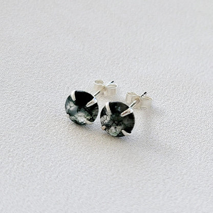 A pair of silver stud earrings with round green moss agate stones. The stones have a marbled pattern from the moss growing through the clear crystal.