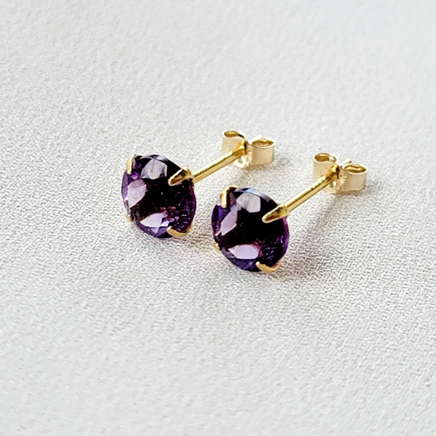 A pair of gold stud earrings with round purple amethyst gemstones