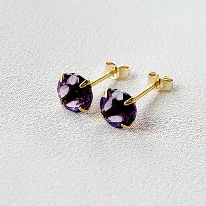 A pair of gold stud earrings with round purple amethyst gemstones