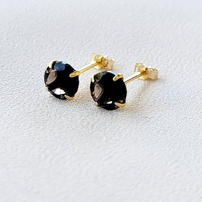 May include: A pair of gold stud earrings with round, dark brown smoky quartz gemstones.