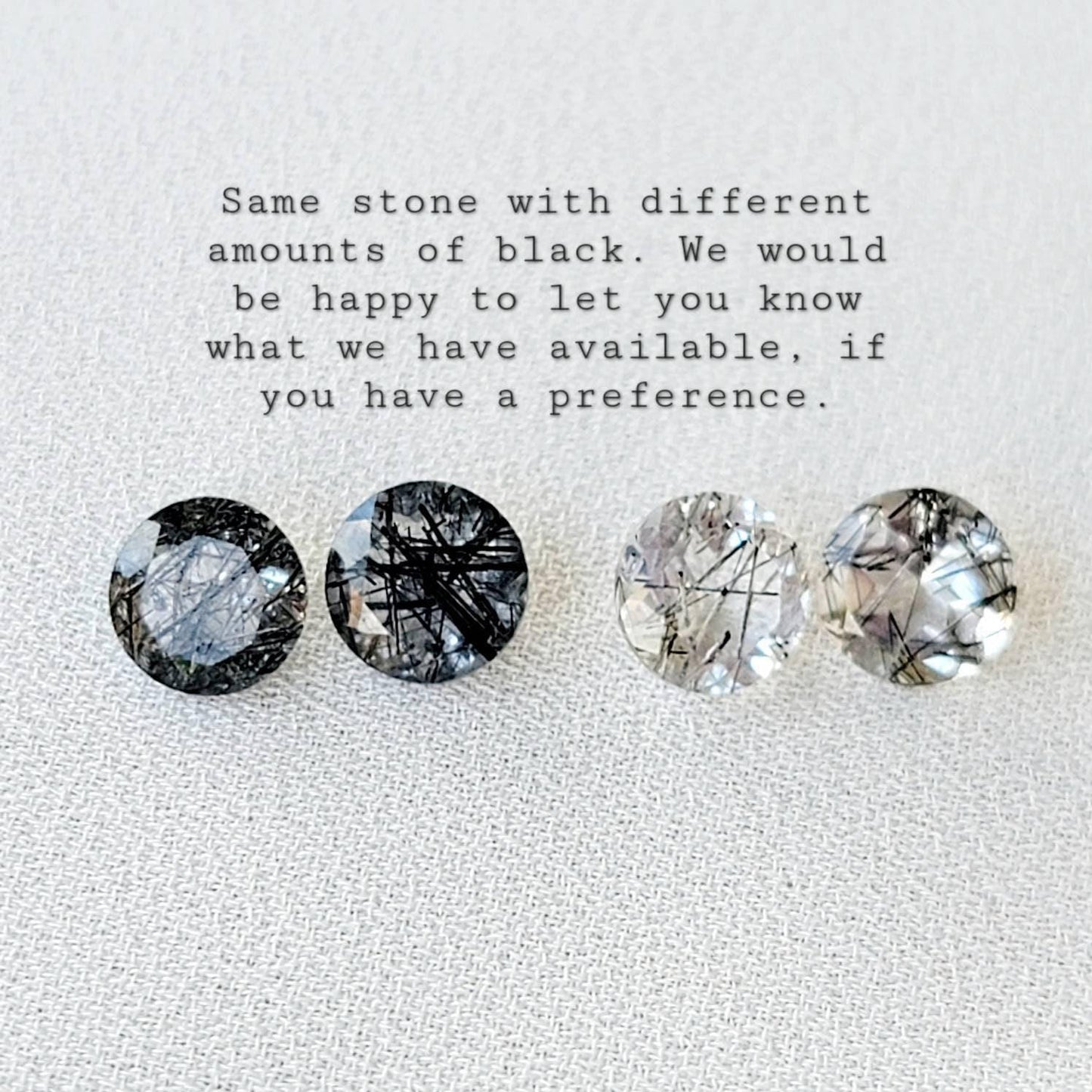 Four round, clear quartz stones with black inclusions. The stones are arranged in a row from left to right. The stones have varying amounts of black inclusions, with the leftmost stone having the most and the rightmost stone having the least. The text &#39;Same stone with different amounts of black. We would be happy to let you know what we have available, if you have a preference.&#39; is above the stones.