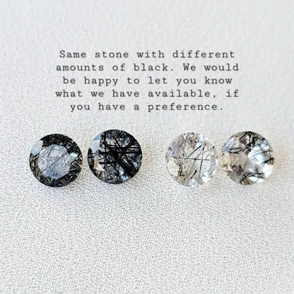 Four round, clear quartz stones with black inclusions. The stones are arranged in a row from left to right. The stones have varying amounts of black inclusions, with the leftmost stone having the most and the rightmost stone having the least. The text &#39;Same stone with different amounts of black. We would be happy to let you know what we have available, if you have a preference.&#39; is above the stones.