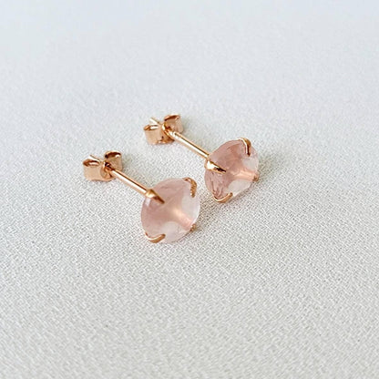 Rose gold stud earrings featuring round faceted rose quartz gemstones. Each earring showcases a light pink, translucent stone securely set in a four-prong rose gold setting. The posts and butterfly backs are also crafted from rose gold, ensuring a cohesive and elegant look. These delicate earrings are perfect for adding a touch of understated glamour to any outfit.