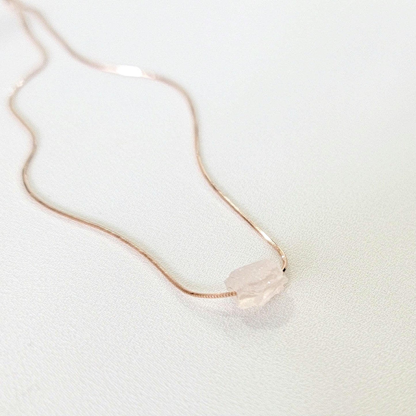 An uncut rough rose quartz stone on a 18k rose gold plated sterling silver necklace. other necklace colors are available.
