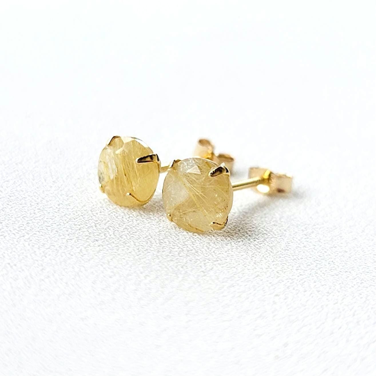 A pair of gold earrings with a clear quartz stone with gold inclusions. The inclusions look like gold spikes that are going through a clear crystal. The stones are round and have a faceted cut.