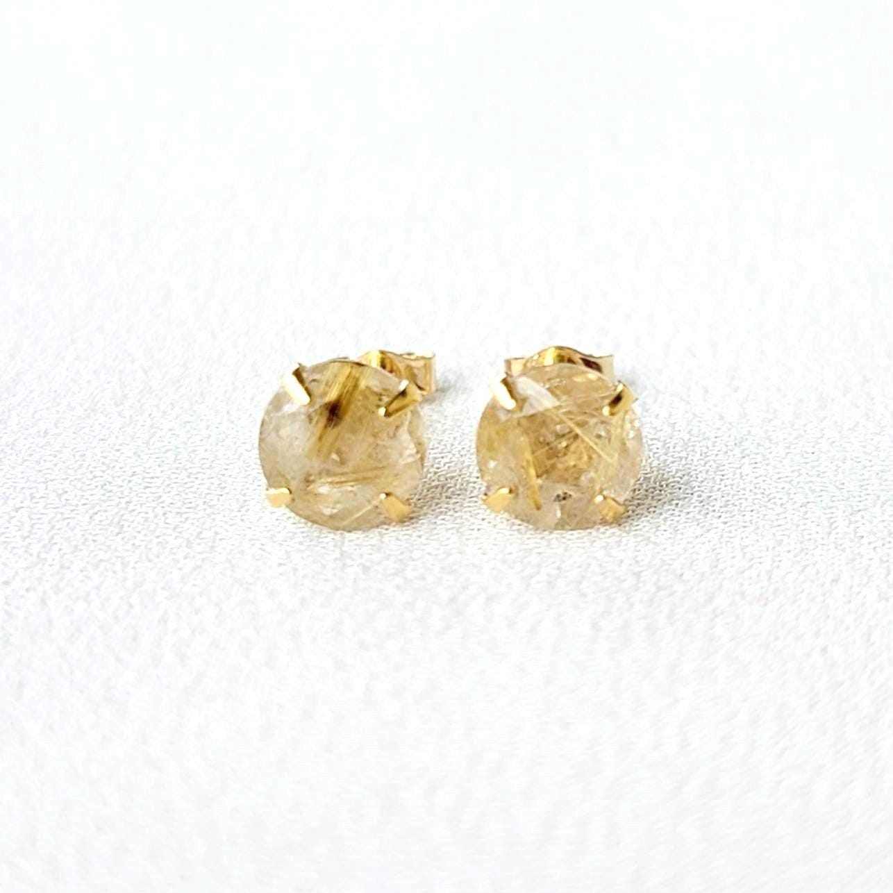 A pair of gold earrings with a clear quartz stone with gold inclusions. The inclusions look like gold spikes that are going through a clear crystal. The stones are round and have a faceted cut.
