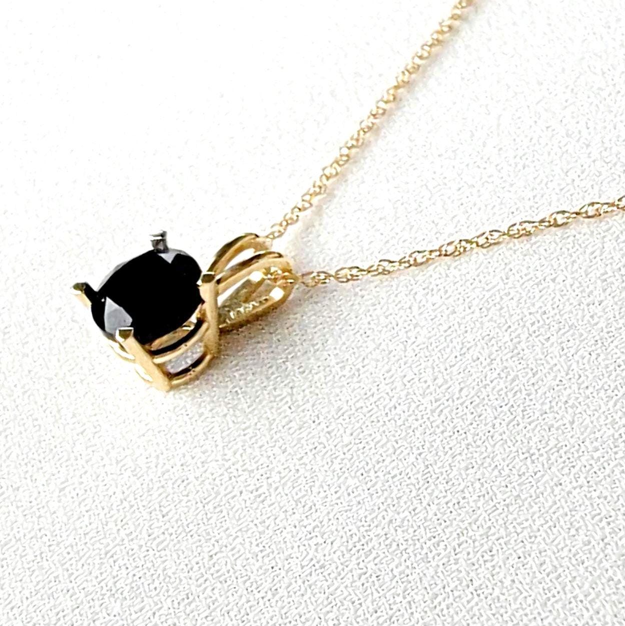 A gold chain necklace with a black gemstone pendant. The pendant is set in a gold setting with a black onyx gemstone.