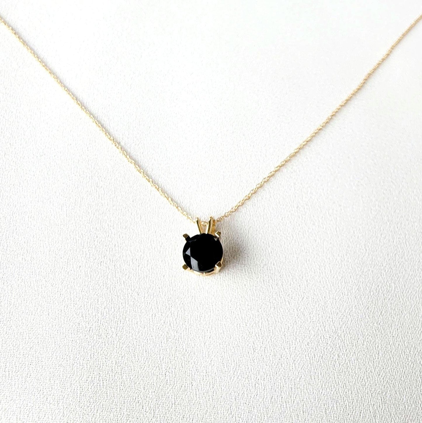 A gold chain necklace with a black gemstone pendant. The pendant is set in a gold setting with a black onyx gemstone.
