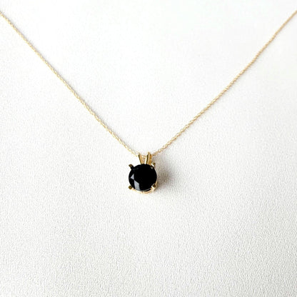 A gold chain necklace with a black gemstone pendant. The pendant is set in a gold setting with a black onyx gemstone.