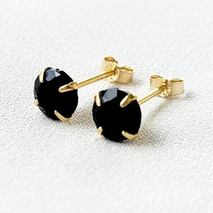 A pair of gold stud earrings with round faceted black onyx gemstones.